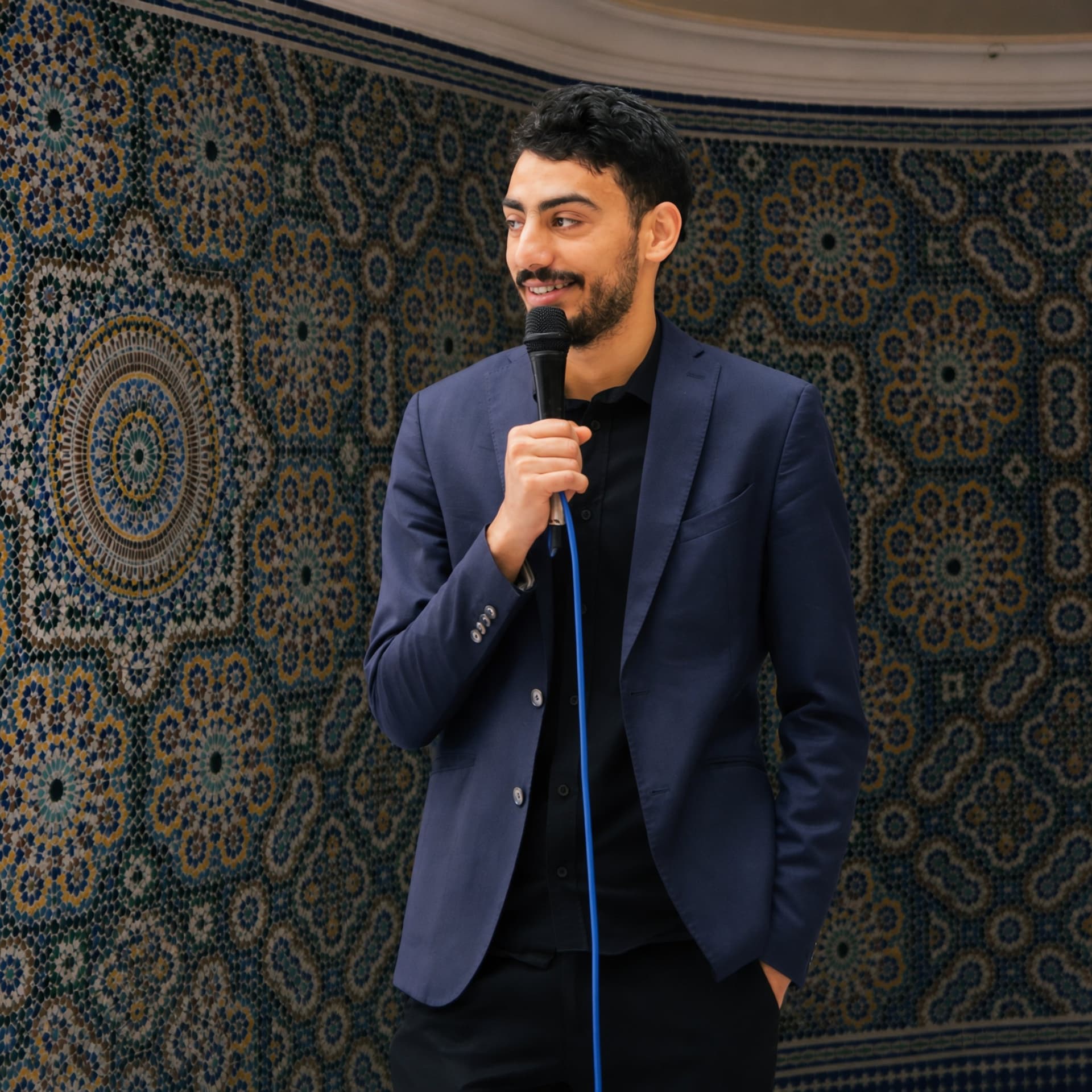 Dhia speaking with a microphone in front of zellige tilework